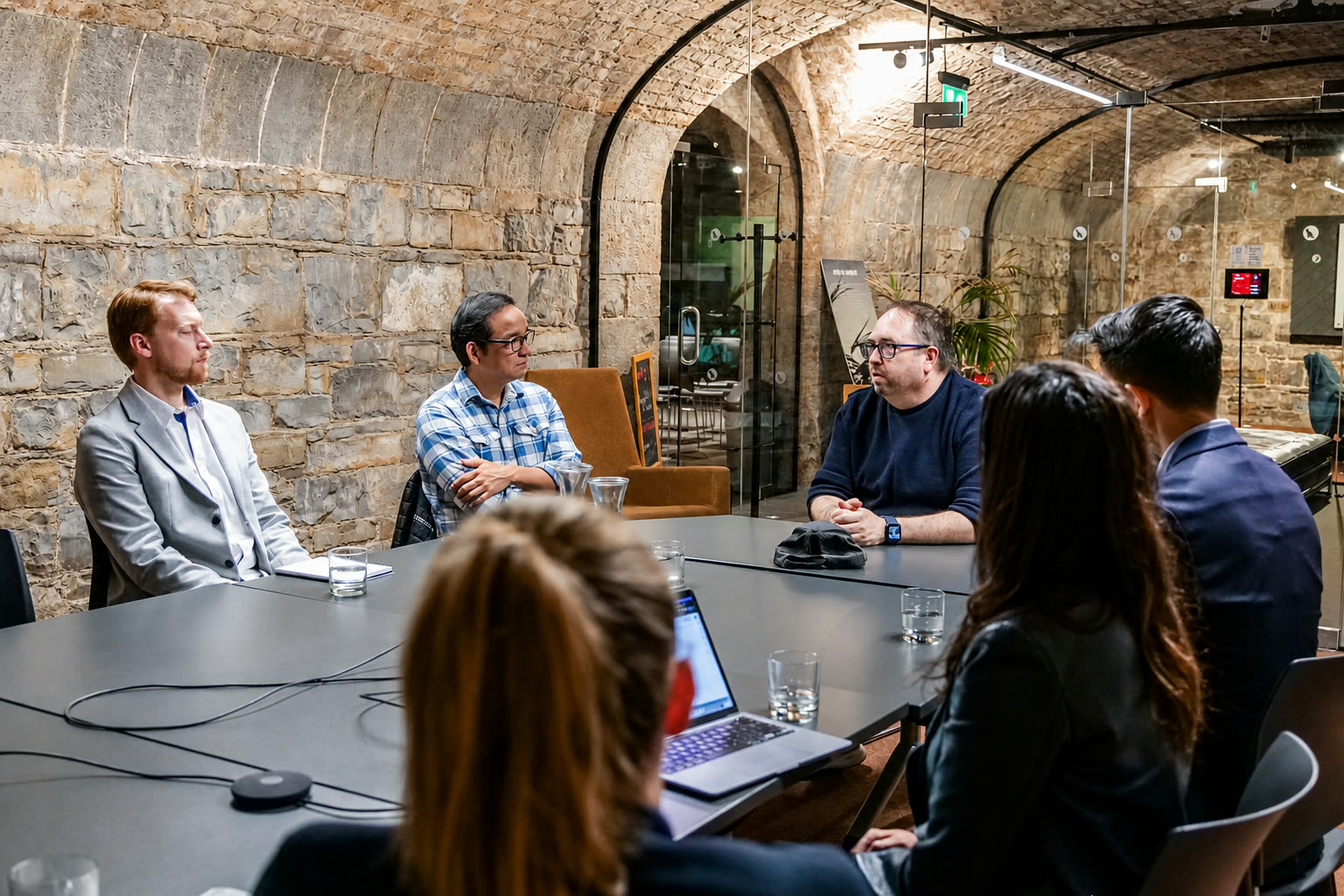 DC leading a small-group pitch review in a stone-vaulted meeting room.