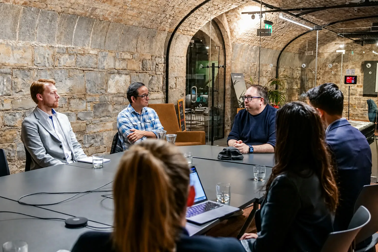 DC leading a small-group pitch review in a stone-vaulted meeting room.